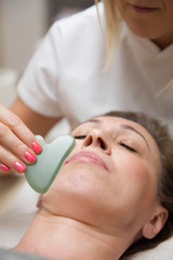 Obraz na płótnie Canvas Woman having an gua sha facial massage with natural jade stone massager