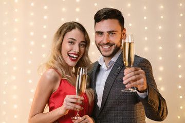 Young happy couple raising champagne glasses and looking at camera