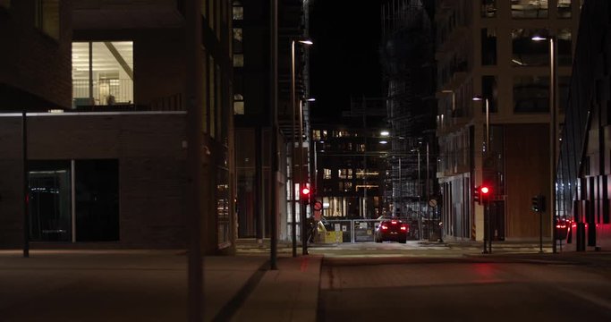 Slow motion close-up to wide 4K shot with parallax motion of illuminated empty downtown street with car parked in intersection in background, at night in Barcode quarter of Bjørvika, Oslo Norway.