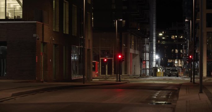 Slow motion close-up to wide 4K shot with parallax motion of illuminated downtown street with public transport bus and cars driving in background, at night in Barcode quarter of Bjørvika, Oslo Norway.