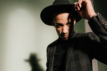 Relaxed african man in elegant jacket expressing interest. Indoor shot of inspired male model standing in dark room.