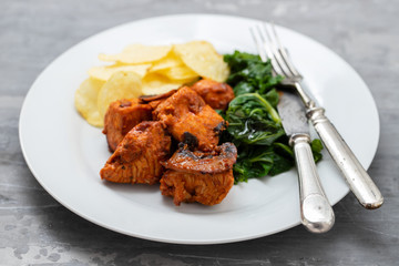 fried meat with potato chips and greens on white plate on ceramic background