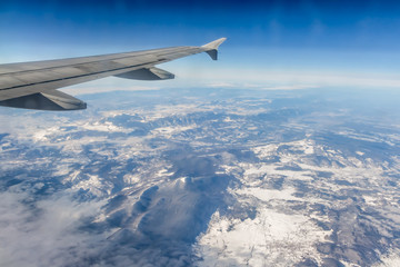 Plane silver wing during a flight over white clouds and a winter land is on the photo