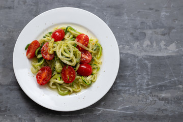 Spiral zucchini noodles with tomato on white plate on ceramic background