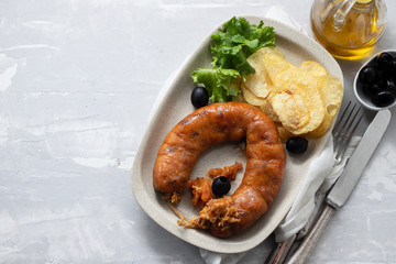 typical portuguese smoked sausage alheira with potato chips and fresh salad on white plate on ceramic background