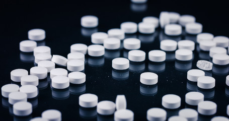 White tablet pills falling down on black background. Medicine and health. Closeup of many medical capsules