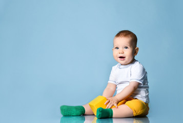 Fototapeta premium Smiling infant baby boy toddler in yellow pants is sitting on the floor holding playing with yellow cube