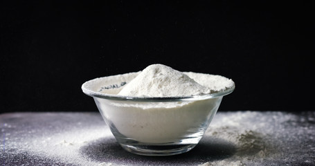 Flour is falling into a bowl in slow motion on black background
