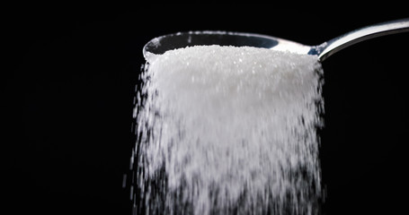 Obraz na płótnie Canvas Sugar or Salt falling off spoon from a bowl at closeup