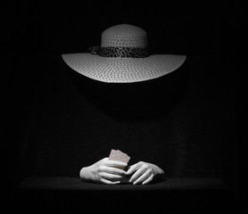 The Ghost of a woman in an elegant hat with playing cards in her hands on a black background. The concept of a card fortune teller or Schuller.