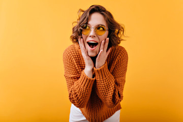 Inspired white female model in vintage sunglasses looking away with surprised smile. Studio shot of...