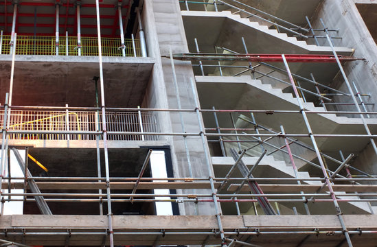 close up of a concrete building under construction surrounded by scaffolding with exposed stairs and floors