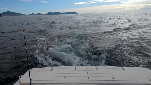 Waves toss and turn a small boat alone in the Sea of Cortez fishing for yellowtail in dark deep waters overlooked by black volcanic cliffs.