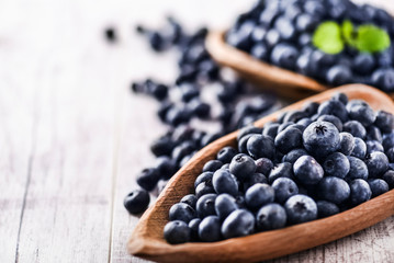 Freshly picked blueberries in wooden bowl on white table. Juicy and fresh blueberry with green leaves at rustic board. Bilberry antioxidant healthy forest food.