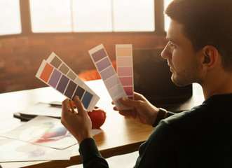 Guy Working With Color Samples Sitting At Laptop In Office