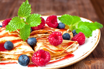 Pile of small homemade pancakes with berries and  syrup on wooden table