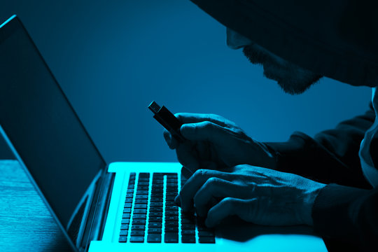 Hacker stealing data from a laptop in a dark room and holding usb memory stick in hand