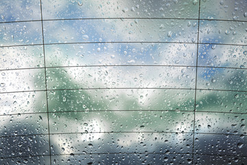 Krople deszczu na tylnej szybie samochodu z chmurami w tle. - obrazy, fototapety, plakaty