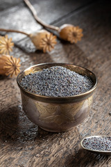 Poppy seeds in a cup with poppy pods in the background