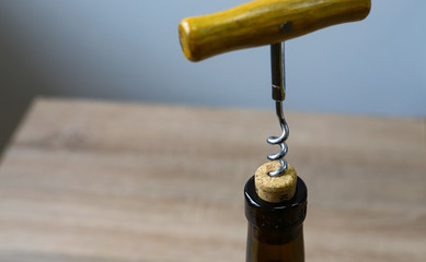 Metal corkscrew with a wooden handle screwed into a bottle stopper with red dry wine. Healthy use...