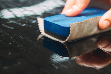 An employee of the car wash thoroughly washes conducts detaling and applies protective equipment to the body of an expensive car.
