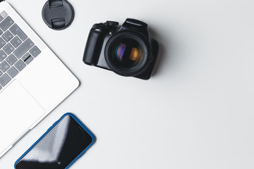 Photographer's workplace on a white background. Modern laptop, digital camera, lens, battery, smartphone. Minimalism. Top view. Copy space. Equipment for the photographer. The concept of freelancing