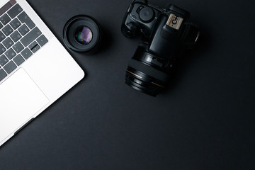 Photographer's workplace on a dark background. Modern laptop, digital camera, lens, battery,...