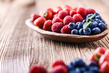 Forest fruits in wooden bowl. Blueberries, raspberries, strawberries on vintage table.