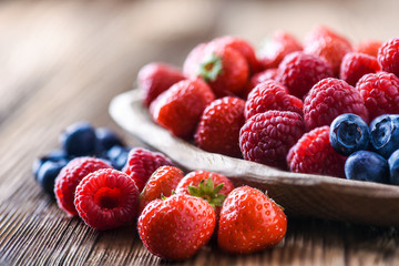 Forest fruits in wooden bowl. Blueberries, raspberries, strawberries on vintage table.