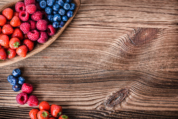 Fototapeta na wymiar Forest fruits in wooden bowl. Blueberries, raspberries, strawberries on vintage table.