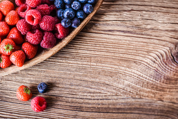 Forest fruits in wooden bowl. Blueberries, raspberries, strawberries on vintage table.