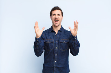 young handsome man furiously screaming, feeling stressed and annoyed with hands up in the air...