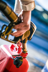 Pour gasoline into canister. Refueling at gas station. Holding a fuel nozzle.