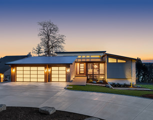 Beautiful modern style luxury home exterior at sunset with glowing interior lights. Features three...