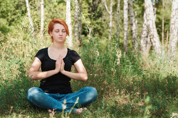 Fototapeta premium Freedom and joyful concept with copy space. Girl teenager meditates in park. Red haired woman sitting on grass.