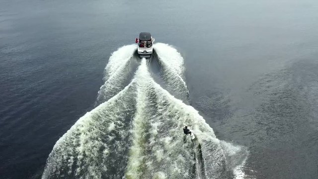 Wakeboarder pulls up and does tricks followed by drone.