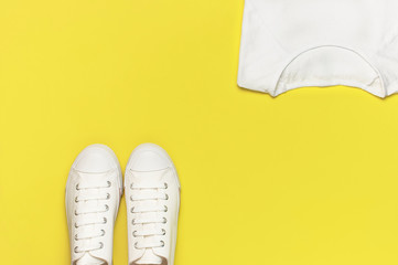 White female fashion sneakers, white T-shirt on yellow orange background. Flat lay top view copy space. Women's shoes. Stylish white sneakers. Fashion blog or magazine concept. Shoe background, sport