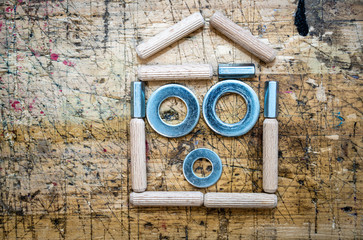 Home shape made with assorted hardware items, nuts, washers and dowels on wooden workbench stained grunge textured surface.