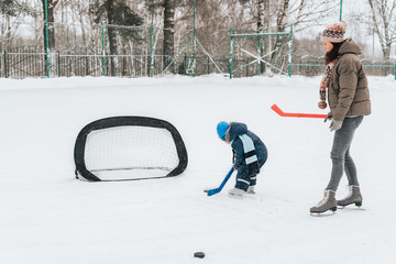 Little funny boy with her mother skating in the park. Play ice hockey with stick and goal. Outdoor....