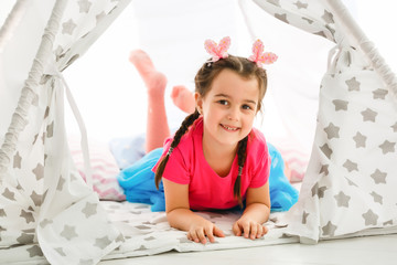 A little girl sits in a wigwam with pillows © Angelov