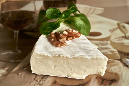  a wooden table with a glass of wine and a piece of Camembert cheese on it The cheese is a creamy white color and is surrounded by a few green leaves The backgroun
