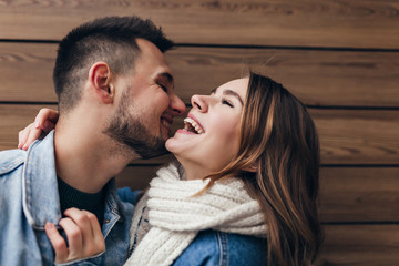 Laughing brunette man expressing love while posing with girlfriend. Blissful caucasian couple kissing on wooden background.