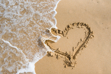 a heart on the sand is washed away by a sea wave