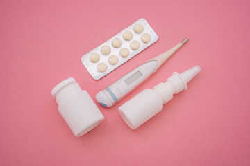 Blister tablets of vitamins pills, tablets, capsules, thermometer and nasal spray on pink background. Pharmacy drugstore and health theme. Selective focus. Virus and flu concept