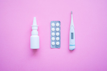 Blister tablets of vitamins pills, tablets, capsules, thermometer and nasal spray on pink background. Pharmacy drugstore and health theme. Selective focus. Virus and flu concept