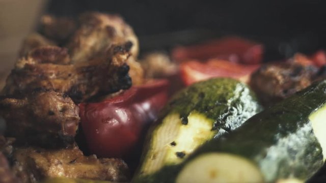 Slow-motion close-up chicken wings and grilled vegetables, (Italian squash and red pepper or red pepper / smoke from the charcoal grill).
