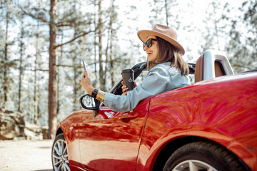 Woman traveling by car in the forest, leaning out of the car window and photographing with a smart phone. Phone with empty screen to copy paste