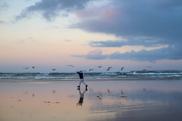 Fototapeta na wymiar boy running with birds in winter beach close to ocean