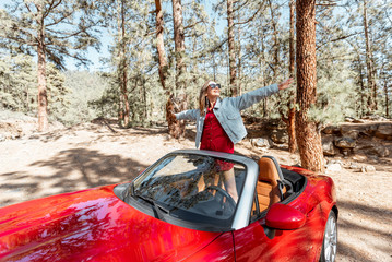 Young stylish woman enjoying traveling by convertible car on nature, pulling hands out of the car....