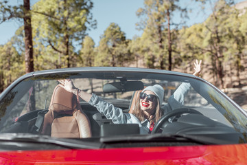 Portrait of a woman driving convertible car while traveling on the forest road, view through the windshield